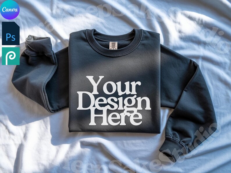 Pode incluir: Um moletom cinza escuro com o texto "Your Design Here" em branco. O moletom est&aacute; colocado sobre uma superf&iacute;cie branca. As mangas est&atilde;o dobradas. A imagem tamb&eacute;m inclui os logotipos Canva, Photoshop e Procreate.