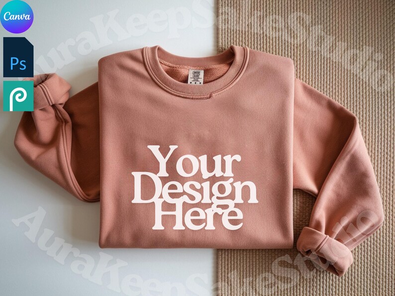 Pode incluir: Um moletom rosa empoeirado com o texto "Your Design Here" em letras brancas. O moletom tem gola redonda e mangas com punhos. O fundo &eacute; de cor neutra.