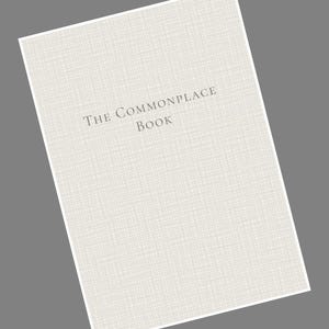 May include: A light-colored book titled "The Commonplace Book" with a textured cover. The book's title is printed in a dark gray font. The book is angled against a gray background.