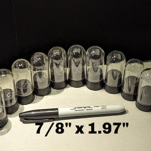 Puede incluir: Un conjunto de cúpulas de vidrio transparente en forma de campana con bases negras. Un rotulador Sharpie blanco está colocado junto a las cúpulas. El texto "7/8" x 1.97"" se muestra debajo. Las cúpulas miden aproximadamente 2,2 cm de ancho y 5 cm de alto.