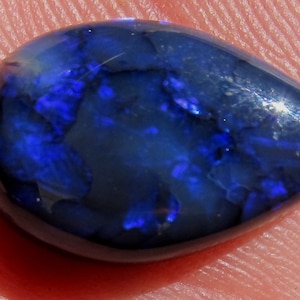 May include: A teardrop-shaped black opal gemstone with a blue and purple iridescent sheen.