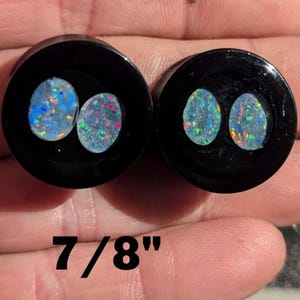 May include: Two black and white round plugs with iridescent opal inserts. The plugs are 7/8 inches in diameter.