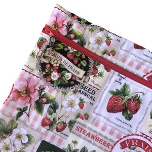 May include: A fabric pouch featuring a vintage-style strawberry and floral print with a red zip closure. A small metal sunflower charm is attached to the zip pull. The pattern includes text such as "LIQUEUR DE FRAISE" and "STRAWBERRY".