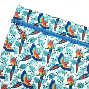 May include: A patterned pouch with a blue zip and a charm. The design features parrots in flight and perched, in red, yellow, and blue, set against a backdrop of tropical leaves and geometric shapes. The zip is blue.
