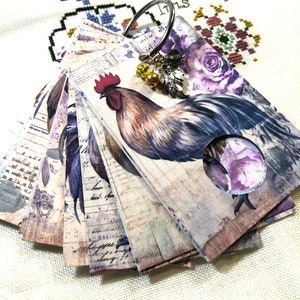 May include: A set of vintage-style cards featuring a rooster illustration with a floral background. The cards are attached to a metal ring with a charm.