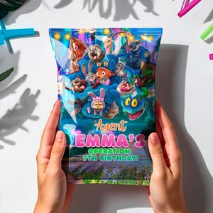 May include: A party bag with the text "Agent Emma's Operation 7th Birthday!" is held by two hands. The bag features cartoon characters and is surrounded by balloons, straws, and tropical leaves. A magnifying glass and a carrot are also visible.