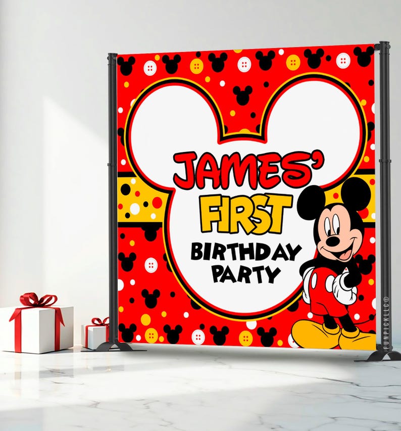 May include: A red backdrop with a Mickey Mouse theme, featuring the text "JAMES' FIRST BIRTHDAY PARTY." The design includes Mickey Mouse ears, polka dots, and a cartoon image of Mickey Mouse. Two white gift boxes with red ribbons are in the foreground.