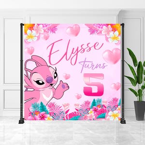 Puede incluir: Un telón de fondo rosa para una fiesta de cumpleaños con el personaje Angel de Lilo & Stitch. El telón tiene el texto "Elysee turns 5" en rosa, con corazones rosas y flores tropicales. Sostenido por un marco de metal negro.