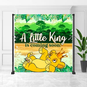 May include: A backdrop featuring a cartoon lion cub wearing a gold crown, with the text "A little King is coming soon!" in white and green. The background has a jungle theme with green foliage and a golden river.