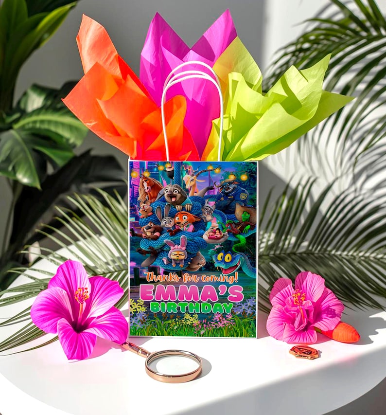 A birthday bag with a colorful design featuring cartoon characters, placed on a table with a pink hibiscus flower, a magnifying glass, and a pink hibiscus.