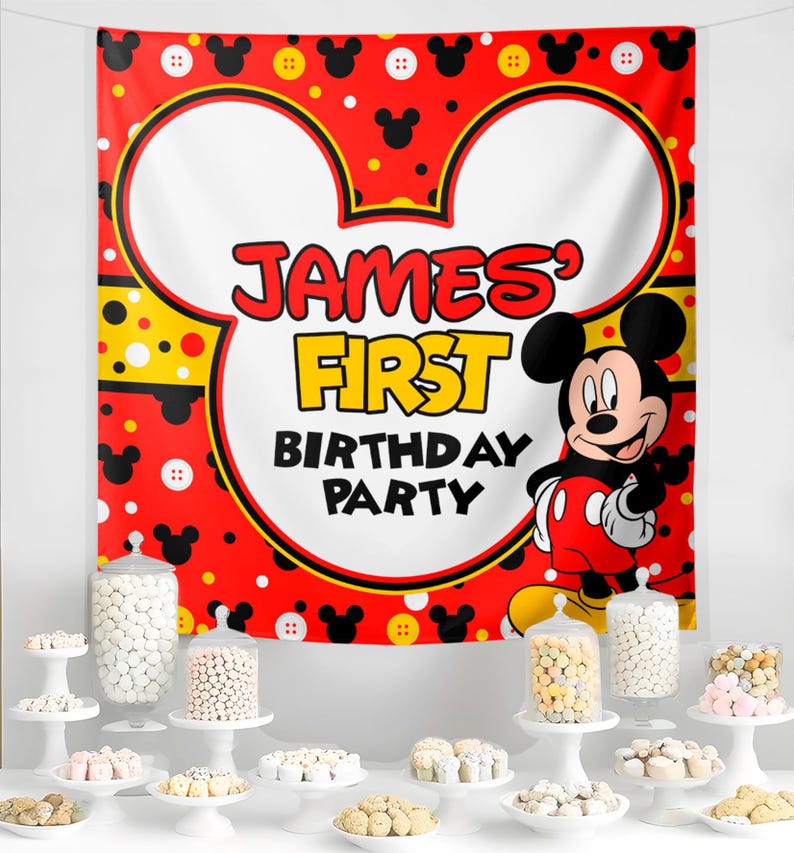 May include: A red and white Mickey Mouse-themed banner with the text "JAMES' FIRST BIRTHDAY PARTY." The banner features Mickey Mouse and decorative elements. Various candies are displayed on white cake stands and in glass jars.