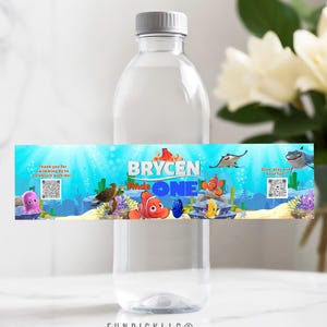 Puede incluir: Una botella de agua de plástico transparente con una etiqueta personalizada con criaturas marinas de dibujos animados y el texto "Brycen Finds One". La etiqueta incluye las frases "¡Gracias por venir a nadar para celebrar conmigo!" y "¡Escanea, juega y diviértete!"
