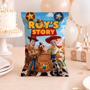 May include: A rectangular snack bag featuring a blue sky background with two gold sheriff badges and the text Roy's Story in yellow and red. The design includes cartoon characters of a cowboy, a cowgirl, and a horse standing on a wooden fence.