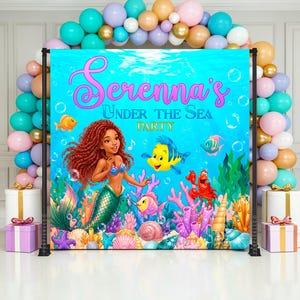 May include: A vibrant backdrop for a party, featuring a mermaid illustration with a teal tail, red hair, and a blue top. The backdrop is set against a blue underwater scene with fish, coral, and the text "Serenna's Under The Sea Party". Balloons in various colors frame the backdrop.