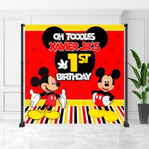 May include: A red and yellow Mickey Mouse themed backdrop for a first birthday party. The backdrop features Mickey Mouse illustrations and the text "Oh Toodles Xavier Jr's 1st Birthday". The design includes black Mickey Mouse ears and a striped border.