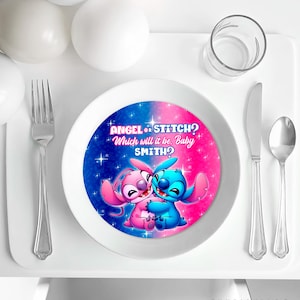Puede incluir: Un plato blanco con un diseño azul y rosa con los personajes Angel y Stitch. El plato tiene el texto "ANGEL or STITCH? Which will it be, Baby SMITH?" y está rodeado de cubiertos y un vaso.