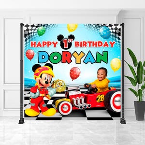 May include: A birthday backdrop featuring Mickey Mouse and a child in a race car. The backdrop has a blue sky background with balloons and the text "Happy 1st Birthday Doryan". The race car is red with the number 28.