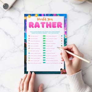 A person's hands are holding a colorful paper with a list of "Would You Rather" questions, and they are writing on it with a pen.