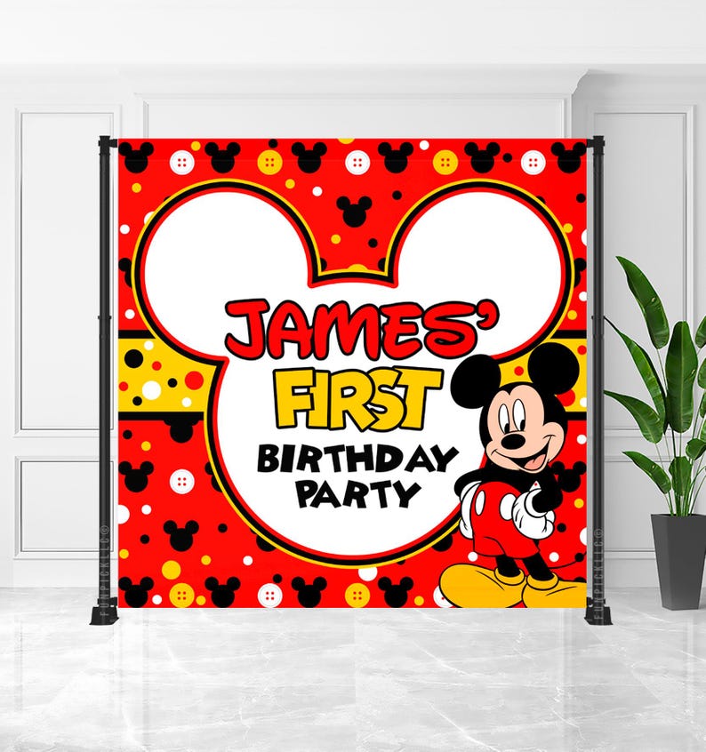 May include: A red backdrop with Mickey Mouse ears and a cartoon image of Mickey Mouse. The backdrop has the text "James' First Birthday Party" in red and yellow. The backdrop is supported by a black metal frame.
