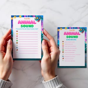A person's hands holding two colorful cards with blank spaces for answers to a "Find the Animal Sound" game.