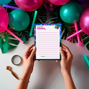 A person's hands holding a blank paper with a message written on it, surrounded by colorful balloons and tropical leaves.