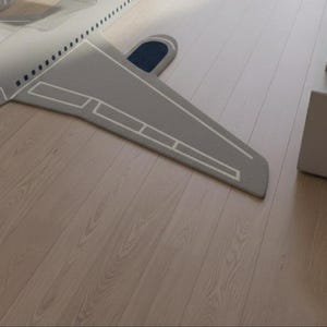 May include: A gray airplane-shaped rug with white outline details and a dark blue accent. The rug is placed on a light-colored wooden floor. The design resembles an airplane wing and tail.