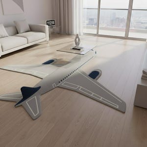 May include: A gray airplane-shaped rug with white trim and navy blue accents. The rug is on a light wood floor in a modern living room. A glass coffee table sits above the rug.