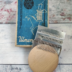 May include: A vintage sewing tool with a wooden base and metal components, alongside a blue box with Cyrillic text and a graphic of a horse and spool. The tool has multiple metal hooks. The box has the word "Шimon" printed on it.