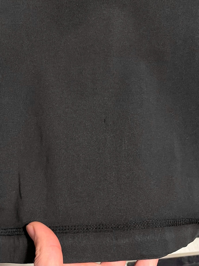 May include: Close-up of a black fabric with a visible texture. The fabric has a smooth appearance with a stitched hem at the bottom. The image shows a small dark spot on the fabric.