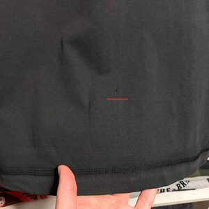 May include: Close-up of a black garment, possibly a shirt or top. The fabric appears smooth with a visible seam at the bottom. The image is well-lit, highlighting the texture and color of the material.