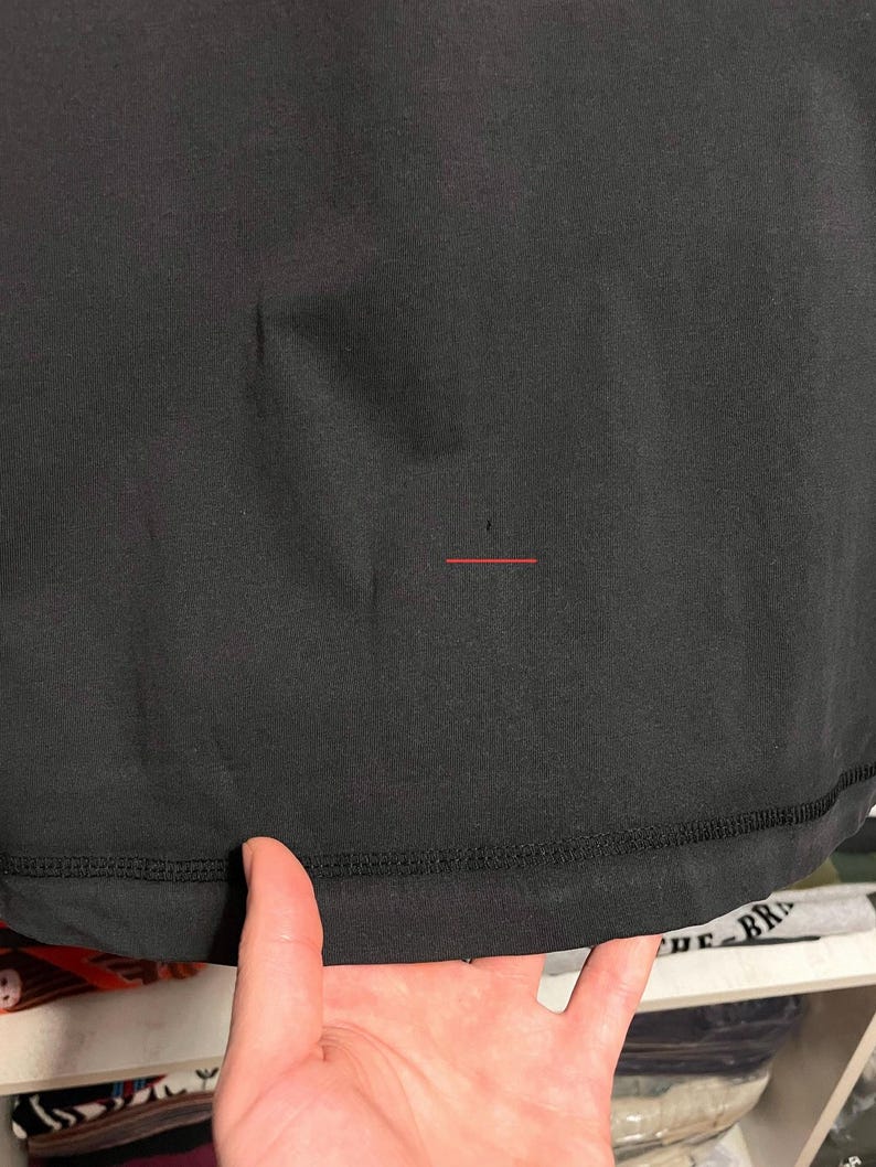May include: Close-up of a black garment, possibly a shirt or top. The fabric appears smooth with a visible seam at the bottom. The image is well-lit, highlighting the texture and color of the material.