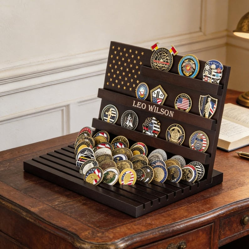 May include: A dark brown wooden coin display stand with multiple shelves, holding a collection of military challenge coins. The stand features a flag design and the name "LEO WILSON". The coins are round, with various colors and designs.