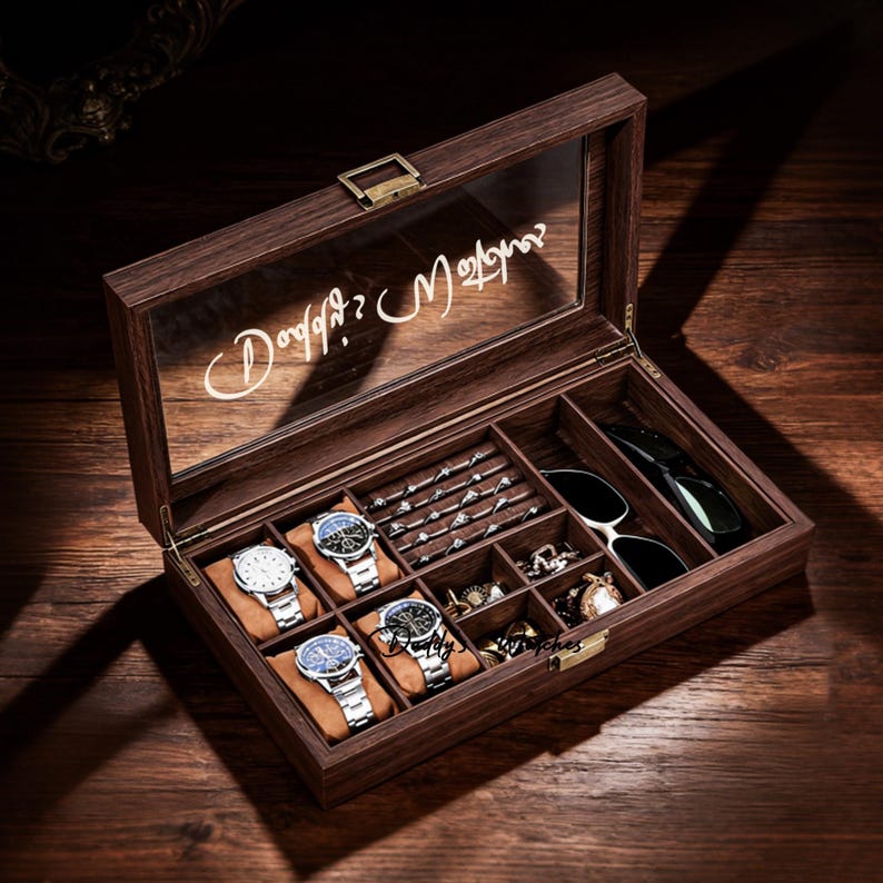 Op de afbeelding: Een donkerhouten horloge- en sieradendoos met een glazen deksel. De open doos onthult compartimenten voor horloges, ringen, armbanden en zonnebrillen. De deksel heeft een cursieve tekst.