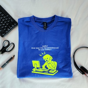 May include: Royal blue t-shirt with the text "Hello! How may I be inconvenienced by you today?" and a graphic of an angry person on the phone at a computer. The graphic and text are in a bright neon green color.