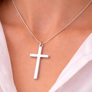 May include: A silver cross pendant necklace. The cross is a simple, polished design suspended from a delicate beaded chain. The necklace is shown against a white background.
