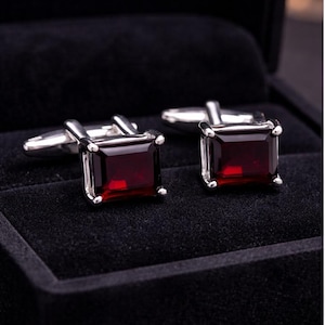 Peut inclure: Paire de boutons de manchette argentés avec des pierres précieuses carrées rouge foncé. Présentés dans un écrin en velours noir, ils mettent en valeur le métal poli et la couleur vive. Les pierres sont taillées à facettes.