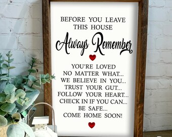 May include: A framed wooden sign with the text "BEFORE YOU LEAVE THIS HOUSE Always Remember" and other inspirational phrases. The sign has a white background with black script and red heart accents. The frame is a dark brown color.