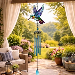 May include: A vibrant stained-glass hummingbird decoration suspended from a chain, above blue wind chimes. The bird is multi-coloured. The wind chimes have long, cylindrical tubes and a teardrop-shaped crystal at the bottom, creating a melodic sound.