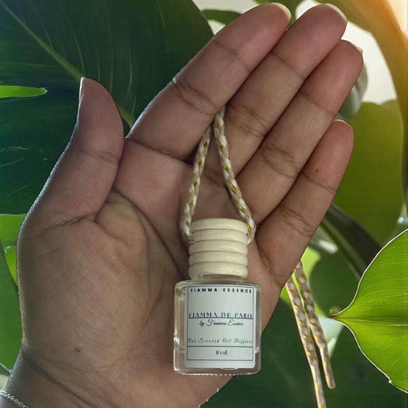 May include: A small, clear glass bottle with a wooden cap and a woven cord. The bottle contains a scented oil diffuser, with the text "FIAMMA ESSENCE" and "FIAMMA DE PARIS" printed on the label. The bottle is 8 ml.