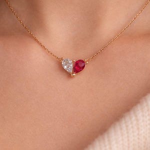 Peut inclure: Un collier en or avec un pendentif en forme de cœur. Le pendentif est composé d'une pierre transparente semblable à un diamant et d'un rubis rouge. Le collier est porté autour du cou.