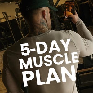 Op de afbeelding: Een persoon draagt een beige shirt met lange mouwen met de tekst "5-DAY MUSCLE PLAN" in het wit. De persoon bevindt zich in een sportschool, houdt een telefoon vast en draagt een groene pet. De achtergrond omvat fitnessapparatuur.
