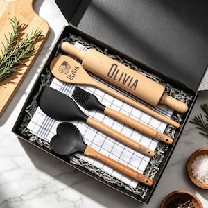 May include: A kitchen utensil gift set in a black box containing a wooden rolling pin, a wooden spoon, a black silicone spatula, a black silicone pastry brush, and a black silicone heart-shaped spoon, all personalized with the name Olivia.