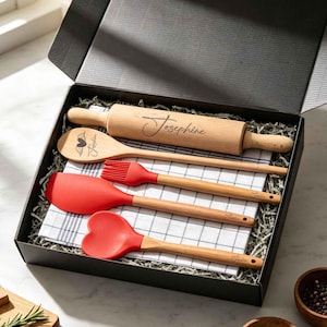 May include: A kitchen gift set in a black box containing a wooden rolling pin engraved with the name Josephine, a wooden spoon with a heart and wing design, a red silicone basting brush, a red spatula, a red heart-shaped spoon, and a plaid towel.