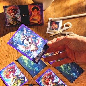 Peut inclure: Plusieurs cartes sur le thème de la fantaisie avec des illustrations de fées et d'un hibou. Les cartes ont des bordures violettes et du texte. Une paire de ciseaux et un crayon sont également visibles.