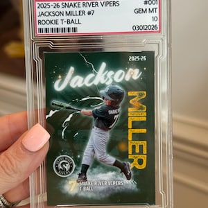May include: A graded 2025-26 Snake River Vipers Jackson Miller #7 rookie T-ball sports card in a clear plastic slab. The card features a green background with a player swinging a bat, the name Jackson Miller, and the team name Snake River Vipers.