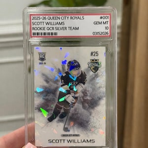 May include: A hockey trading card encased in a protective holder. The card features a player in a black and white uniform with the text "SCOTT WILLIAMS" and "QUEEN CITY ROYALS". The card is graded as GEM MT 10.