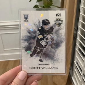 May include: A hockey trading card featuring Scott Williams of the Queen City Royals. The card has a holographic design with the team logo and player's name. The card is encased in a protective sleeve.