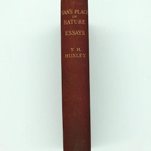 Puede incluir: Un libro antiguo titulado "Man's Place in Nature Essays" de T. H. Huxley. El libro tiene una cubierta de color marrón rojizo oscuro con letras doradas. La columna vertebral muestra signos de desgaste, lo que indica su edad.