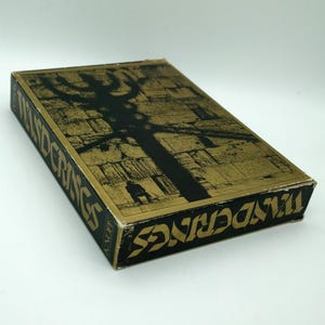 May include: A rectangular book titled "The Wanderings" with a black and gold cover. The cover features a black tree-like silhouette against a gold textured background. The book's spine and edges also display the title.