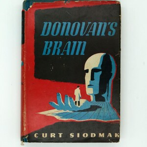 May include: Vintage paperback book cover for "Donovan's Brain" by Curt Siodmak. The cover features a striking illustration with a red and black background, blue text, and a stylized human figure with a brain. The book is a science fiction novel.